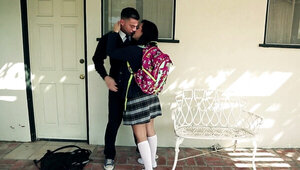 A black haired girl is getting kissed in the yard by her schoolmate